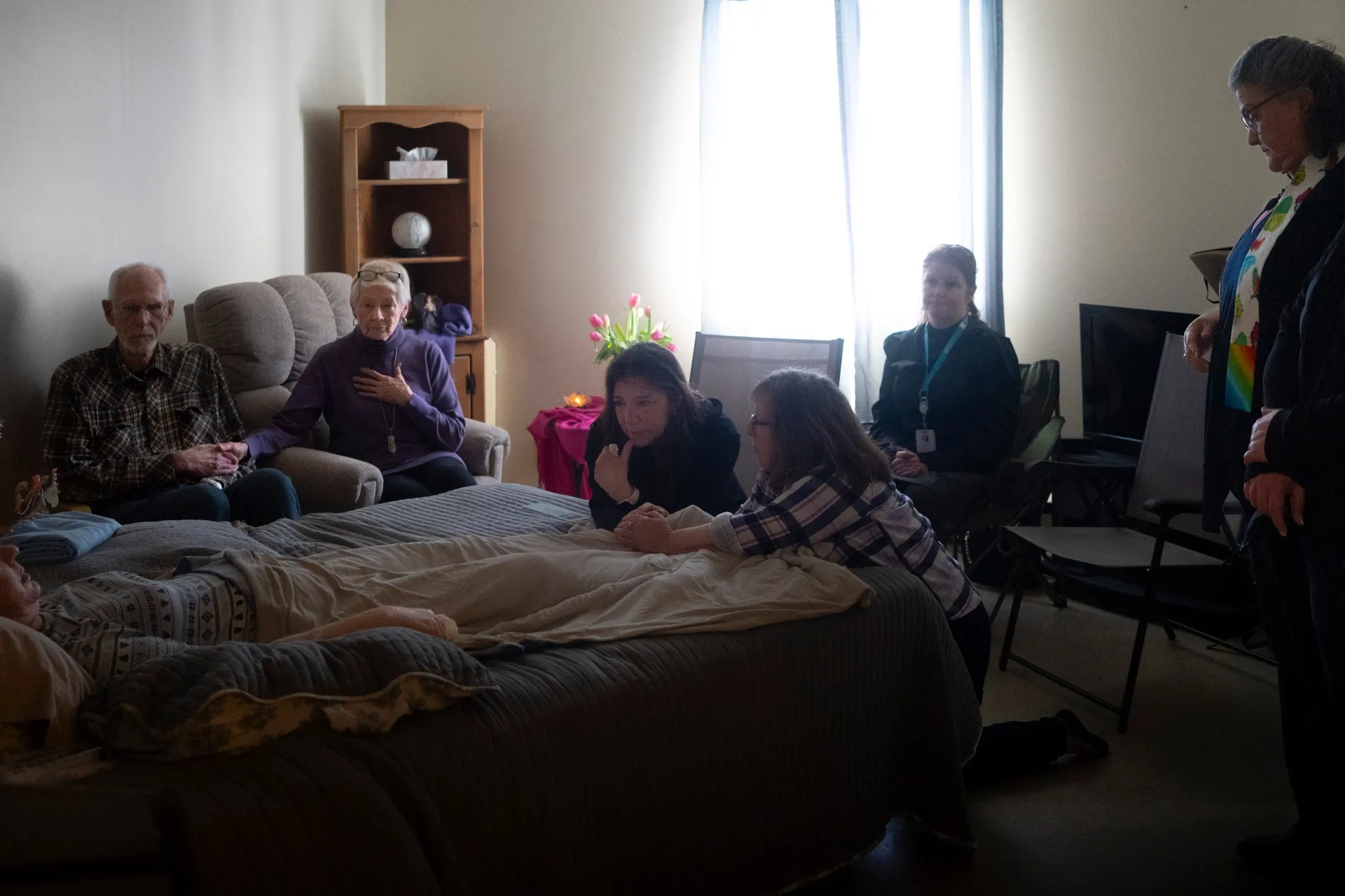 In Paula’s final moments, the room was still. Her childhood friend knelt at the foot of the bed, joined by her death doula.